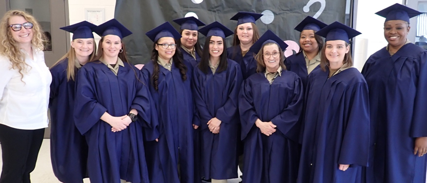 Group of graduates and their instructor pose for a photo in cap and gown.